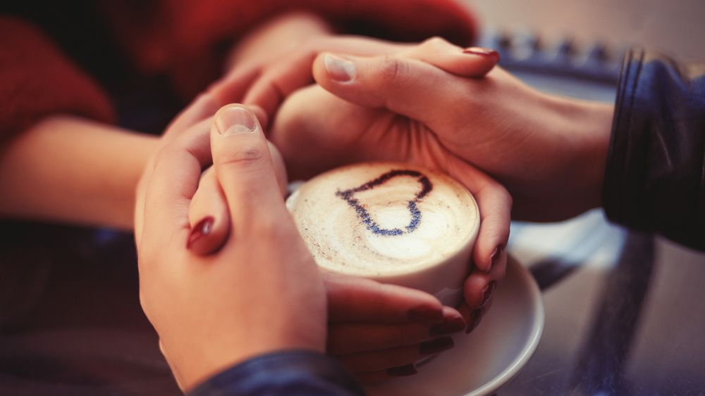 Обои для рабочего стола Девушка с парнем сидят в кафешке и греют руки о чашку с кофе, с сердечком на кофе