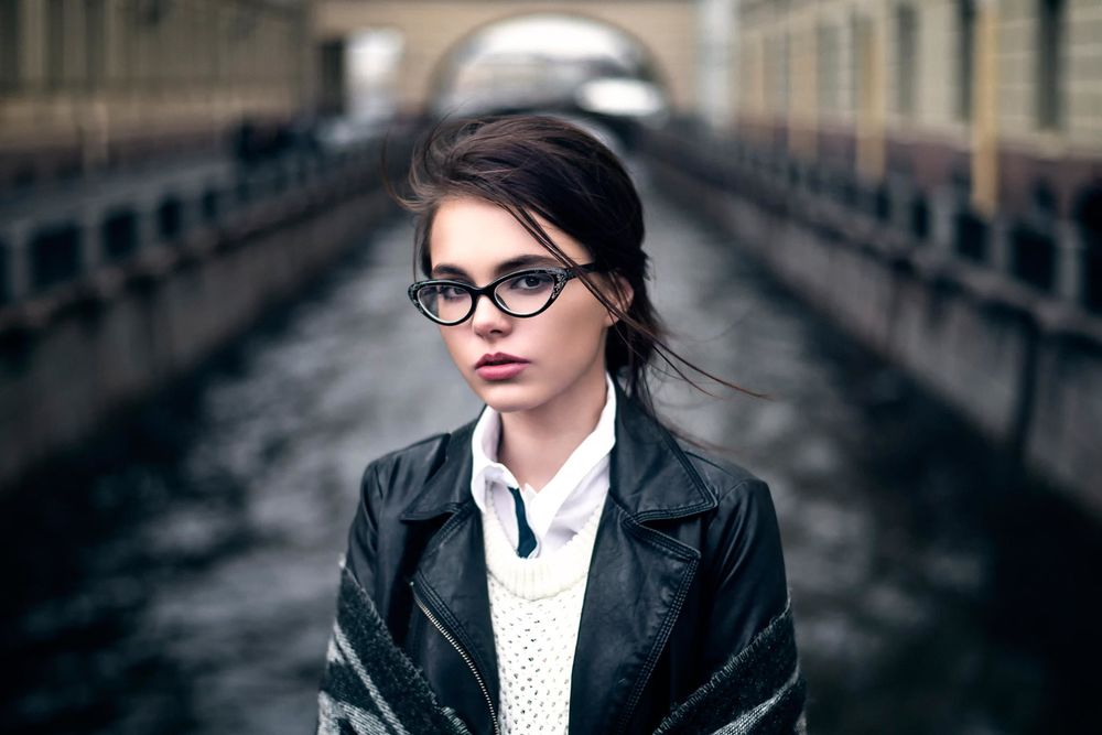 Обои для рабочего стола Красивая девушка Октябрина Максимова в очках и кожаной куртке стоит на мосту на фоне канала или реки