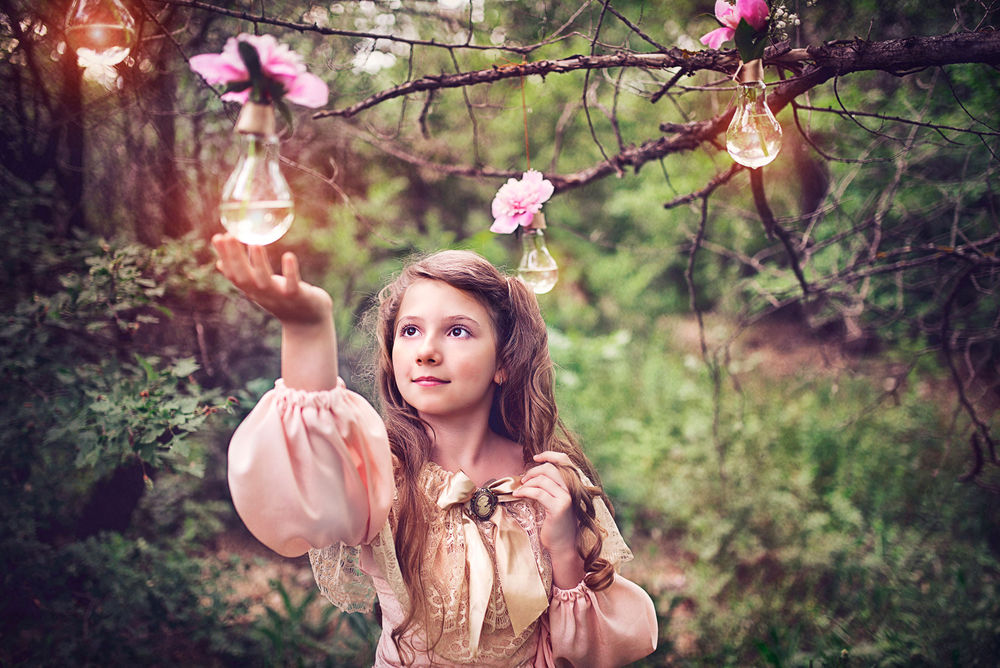 Обои для рабочего стола Милая девушка в красивом, бежевом платье, притрагивается к лампочке с цветком, прикрепленной к ветке дерева