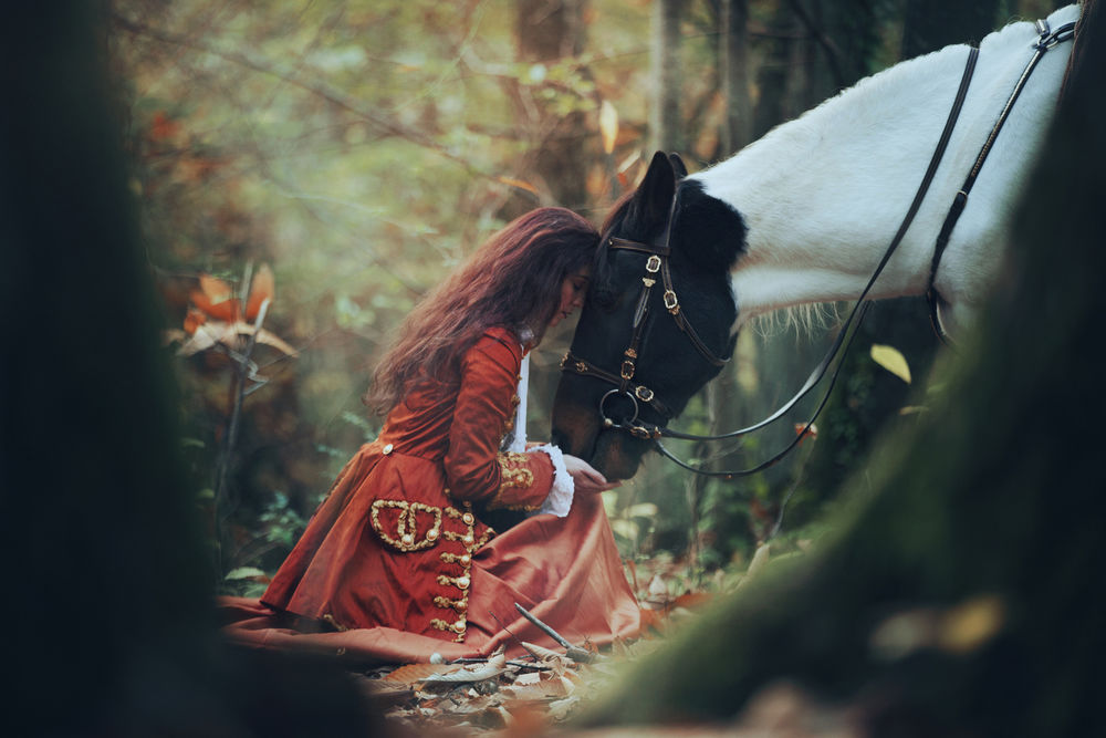 Обои для рабочего стола Девушка, в военном красном мундире, сидит в лесу, приложив свою голову к голове лошади