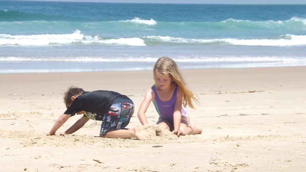 Обои для рабочего стола Дети на пляже, строят замок из песка на фоне моря