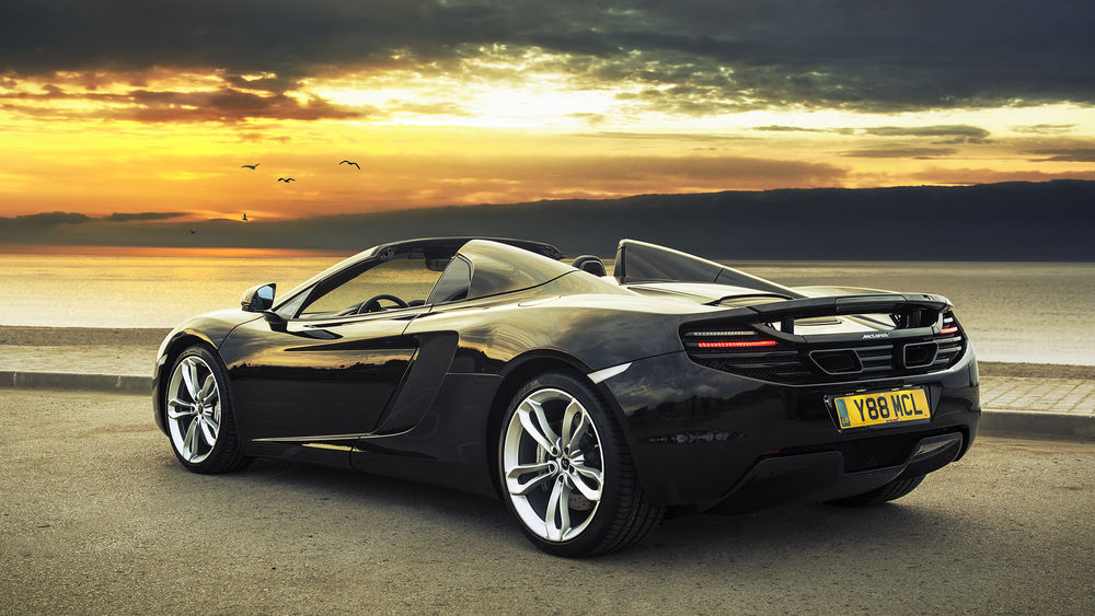Обои для рабочего стола Автомобиль марки McLaren MP4-12C, стоит на дороге на фоне залива и неба озаряемого закатом