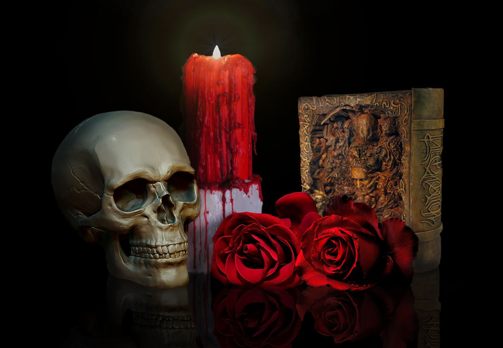 Обои для рабочего стола Череп лежит рядом с горящей свечой, красными розами и книгой на черном фоне