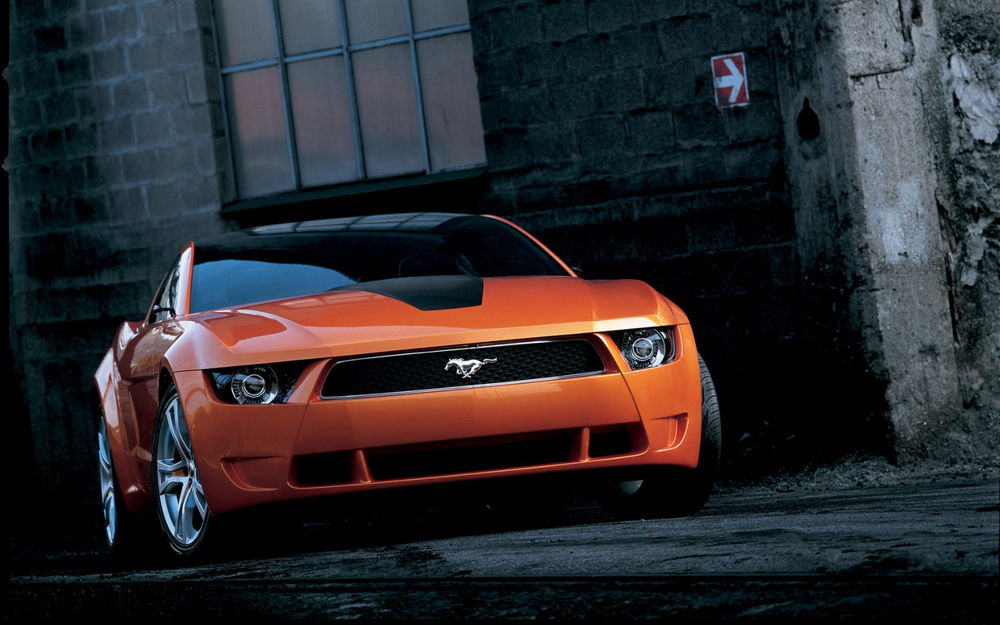 Обои для рабочего стола Оранжевый автомобиль марки Giugiaro Ford Mustang, припаркован рядом с домом