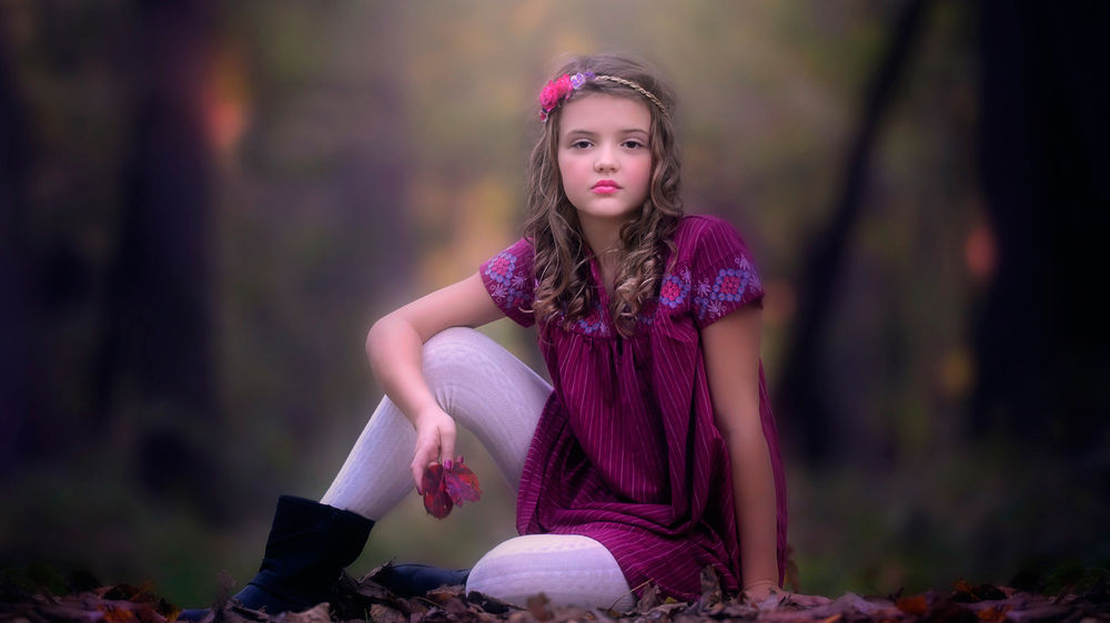 Обои для рабочего стола Девочка в бордовом платье сидит на земле в опавших листьях на фоне природы