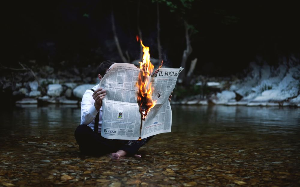 Обои для рабочего стола Парень сидит в воде и читает горящую газету