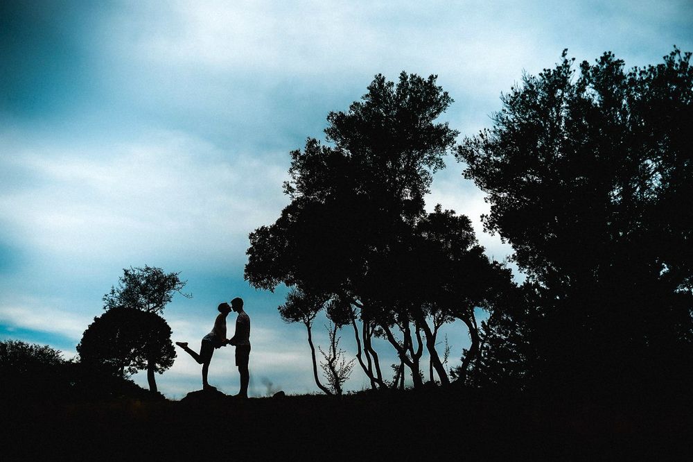 Обои для рабочего стола Парень и девушка целуются на фоне деревьев и синего неба с белыми облаками, фотограф Евгений Малдованов
