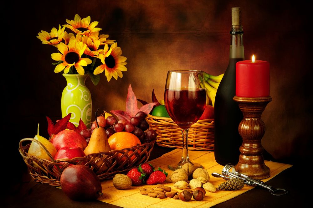 Обои для рабочего стола Букет с ромашками на столе, заставленном корзинами с фруктами, зажженной свечой в подсвечнике, бутылкой вина, бокалом с вином, орешками, штопором