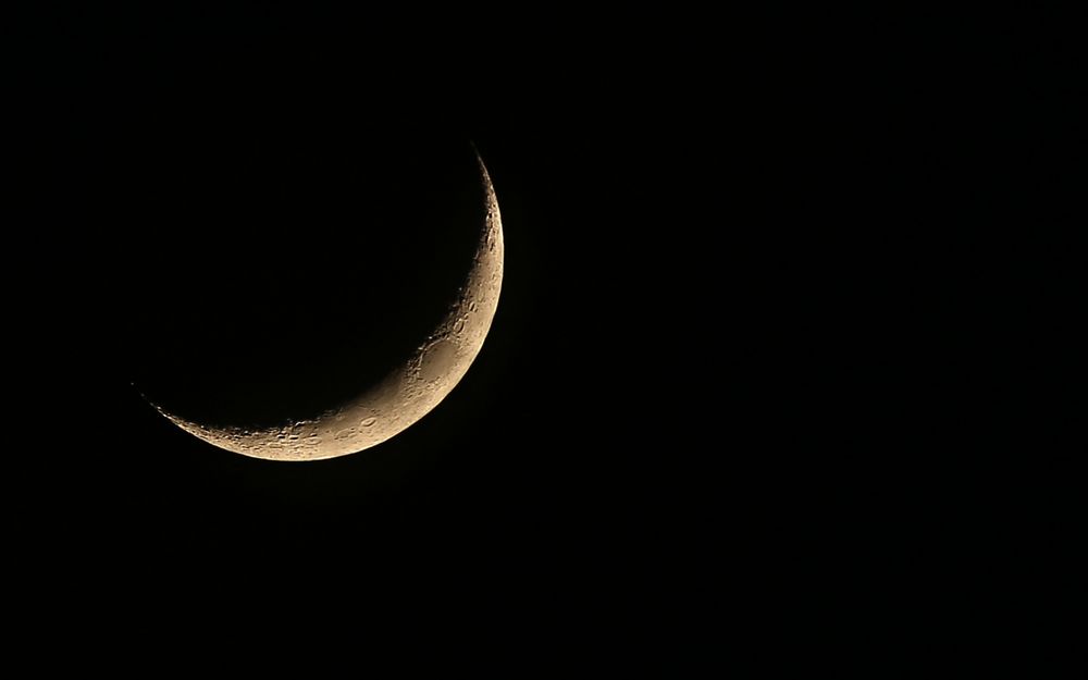 Обои для рабочего стола Освещенная часть Луны в космосе