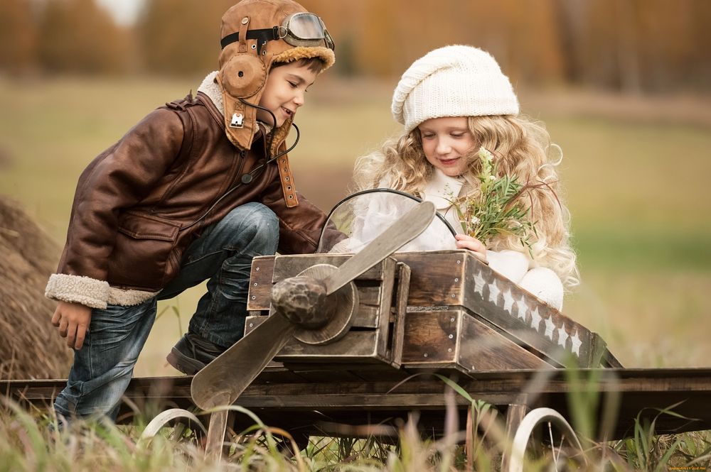 Обои для рабочего стола Мальчик в костюме пилота учит девочку сидящую в игрушечном самолете, на фоне осеннего леса и поля