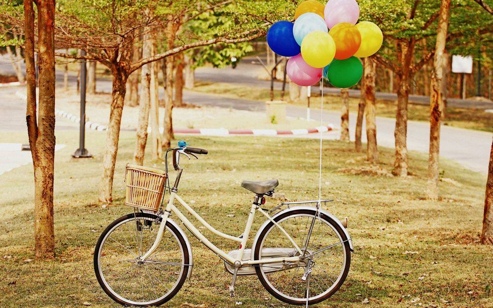 Обои для рабочего стола Велосипед с разноцветными шариками стоит среди деревьев