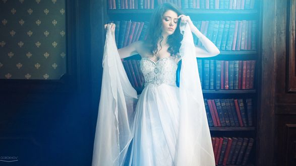 Обои на рабочий стол Девушка в белом платье стоит на фоне книжных полок, фотограф Иван Горохов / Gorokhov