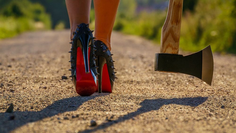 Обои для рабочего стола Девушка идет по дороге (видны только ноги в черных туфлях с шипами) с топором в руке