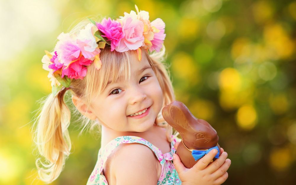Обои для рабочего стола Девочка в веночке из роз держит в руке шоколадного зайца и улыбается