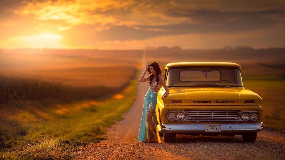 Обои на рабочий стол Девушка в бирюзовом платье со стразами стоит на дороге  возле желтой машины в поле на закате, обои для рабочего стола, скачать  обои, обои бесплатно