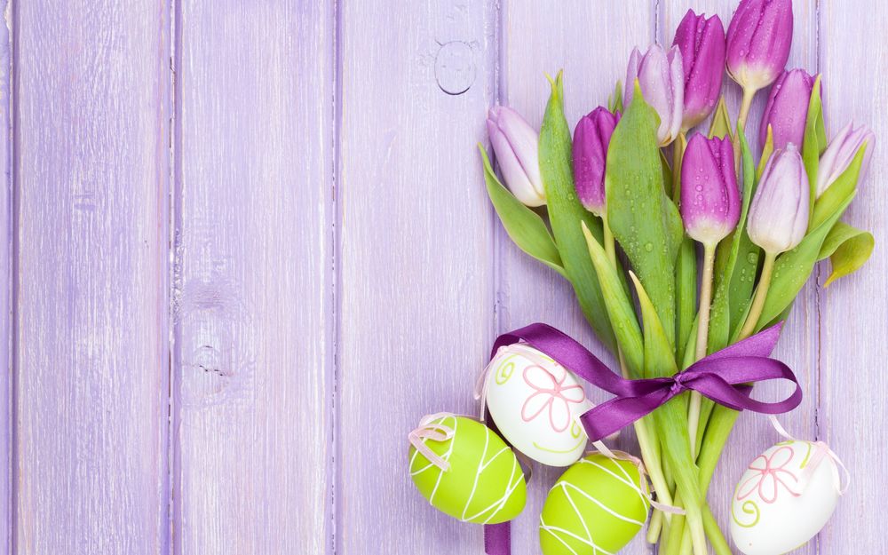 Обои для рабочего стола Фиолетовые и сиреневые тюльпаны, перевязанные бантом, рядом с пасхальными яйцами, на фоне сиреневых досок