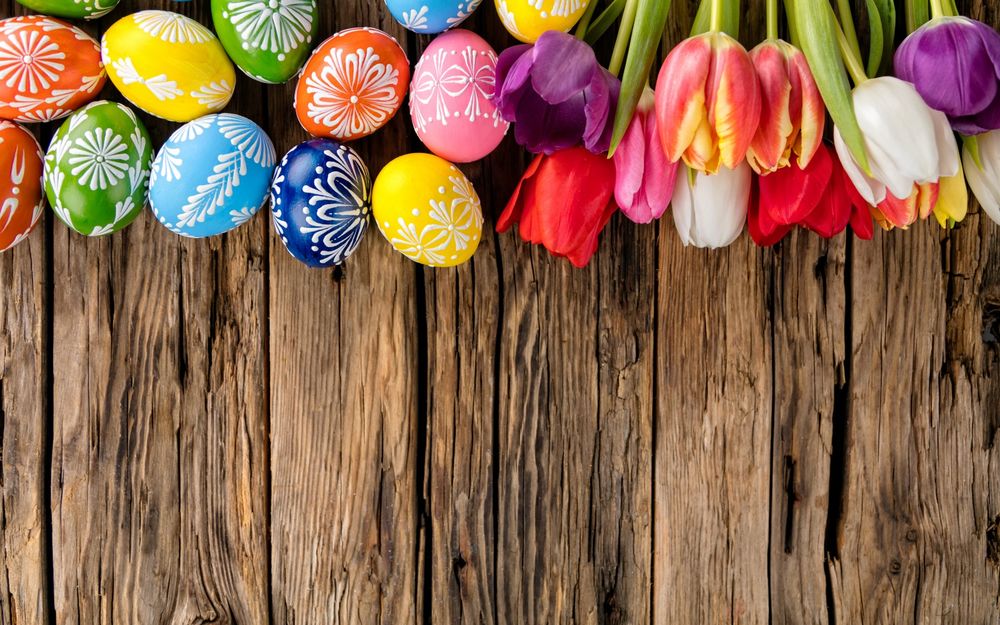 Обои для рабочего стола На деревянных доках лежат цветные пасхальные яйца и цветные тюльпаны, в честь праздника Великой Пасхи