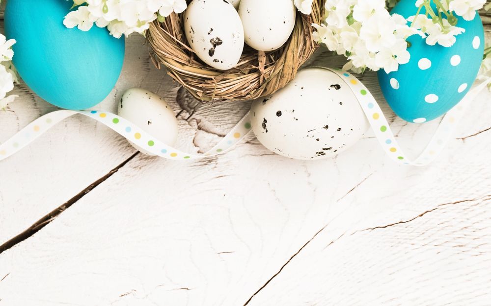 Обои для рабочего стола Перепелиные яйца в гнездышке, рядом куриное пятнистое яйцо, голубые крашеные яйца, лента и цветы, на дощатой поверхности