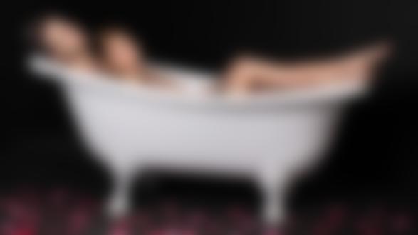Обои для рабочего стола Влюбленная пара лежит в белой ванне, на полу рассыпаны лепестки роз, на черном фоне
