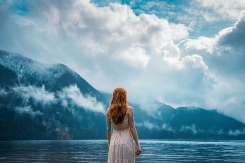 Обои на рабочий стол Девушка стоит к нами спиной на фоне гор у воды, by Lizzy Gadd