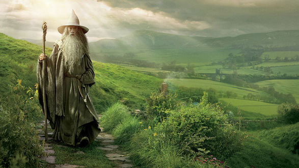 Обои на рабочий стол Гэндальф / Gandalf идет по тропе среди залитых солнцем лугов, из фильма Хоббит: Нежданное путешествие
