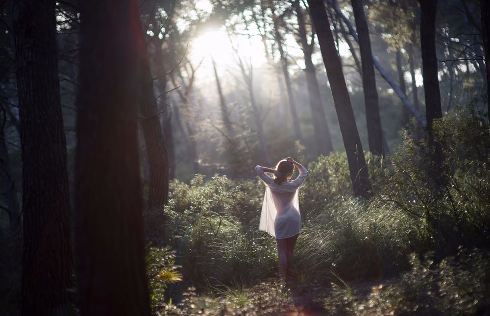 Обои для рабочего стола Девушка в прозрачной рубахе идет по летнему утреннему лесу, залитому солнечным светом, подняв руки к голове