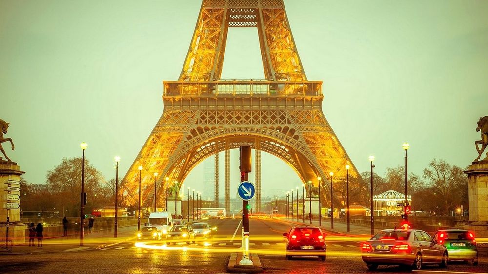 Обои для рабочего стола Дождливый вечер в Париже / Paris, вид улицы с фрагментом Эйфелевой башни, авто, пешеходами, горящими фонарями и деревьями
