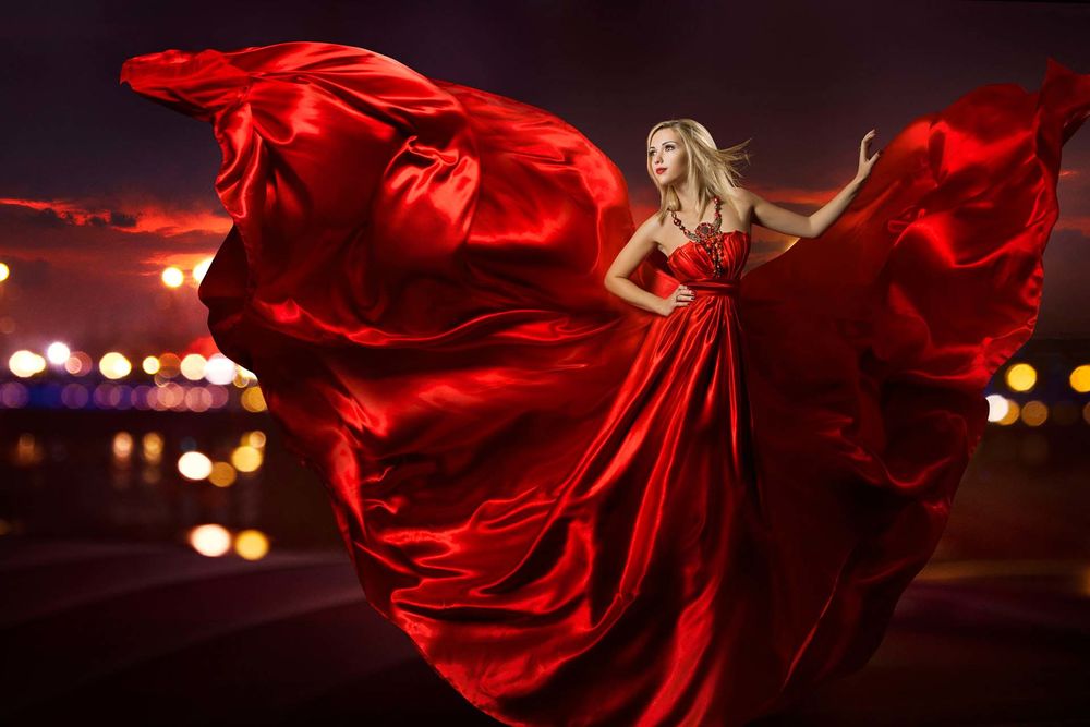 Обои для рабочего стола Девушка блондинка в развевающемся красном шелковом платье стоит на фоне огней, Jerry Ghionis