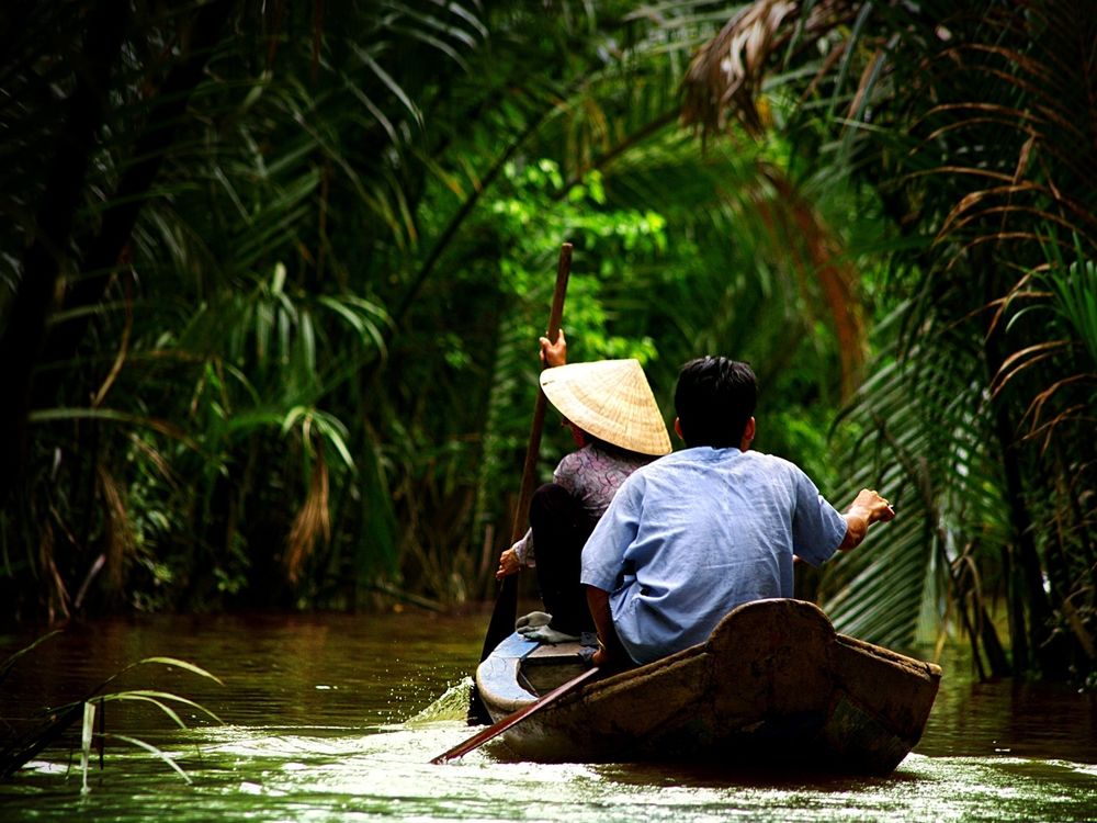 Обои для рабочего стола Мужчины плывут в лодке по реке среди тропического леса