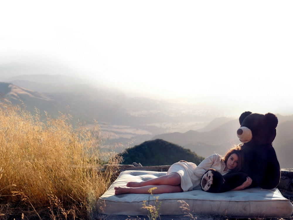 Обои для рабочего стола Девушка лежит на матрасе, обнимая большого плюшевого медведя, вокруг красивый утренний пейзаж