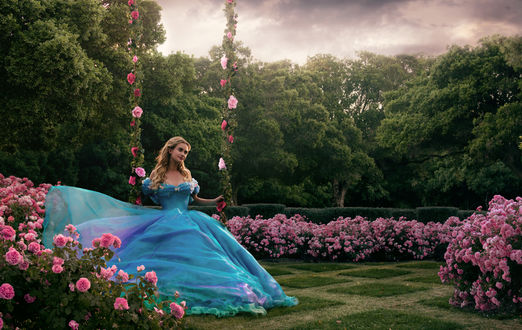 Обои на рабочий стол Актриса Лили Джеймс / Lily James в роли Золушки / Cinderella из одноименного фильма сказки в голубом пышном платье сидит на качели в цветочном саду, by michellemonique