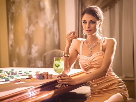 Обои на рабочий стол Девушка в красивом платье пьет коктейль, сидя возле игорного стола в казино