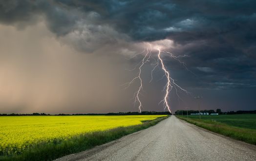 Обои на рабочий стол Дорога, идущая вдоль зеленого поля, в конце которой бьет молния и собираются тучи
