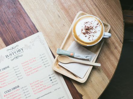 Обои на рабочий стол На деревянном столе лежит меню кафе B-Story coffee, стоит кофе капучино, деревянная ложечка и сахар