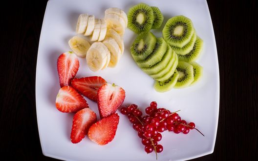 Обои на рабочий стол Нарезанные фрукты и ягоды на тарелке: киви, банан, смородина и клубника