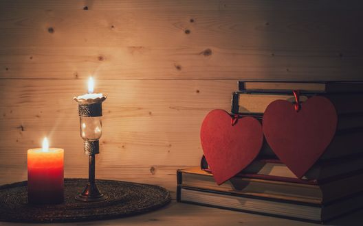 Обои на рабочий стол На стопке книг висят два красных сердца, рядом горят две свечи