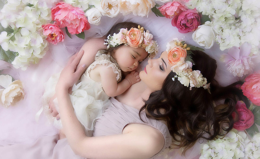 Обои для рабочего стола Молодая мама лежит в постели усыпанной розами с маленькой дочкой, у обоих веночки из роз на голове