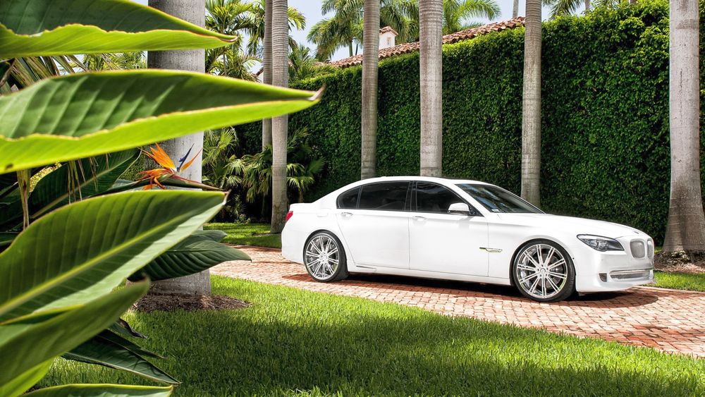 Обои для рабочего стола Белый автомобиль BMW / БМВ во дворе богатого особняка, на фоне увитой плющом стены, на переднем плане листья тропического растения