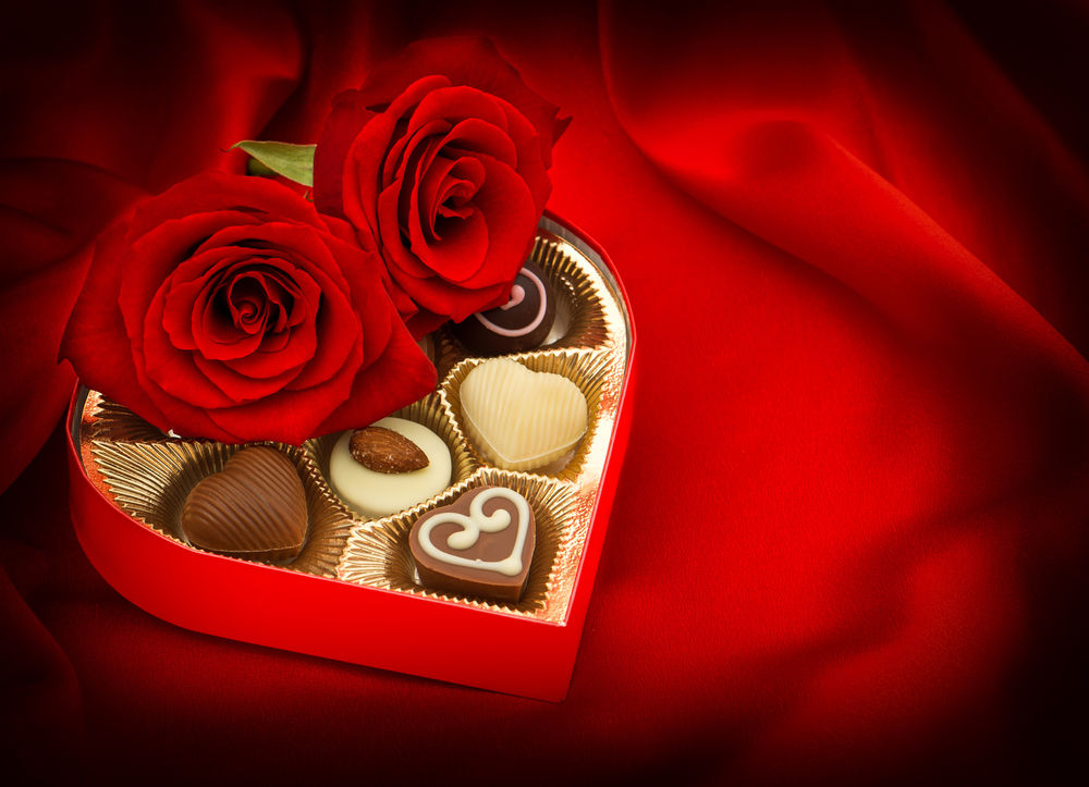 Обои для рабочего стола Две розы, лежащие поверх коробки с конфетами в форме сердца