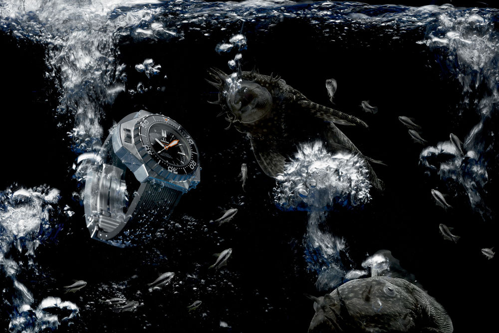 Обои для рабочего стола Наручные мужские часы с браслетом фирмы OMEGA, опускаются под воду с пузырьками воздуха, сопровождаемые рыбами