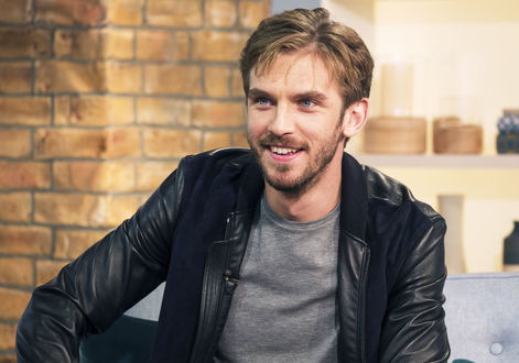 Обои на рабочий стол Английский актер Dan Stevens / Дэн Стивенс в кожанной куртке сидит на фоне декораций