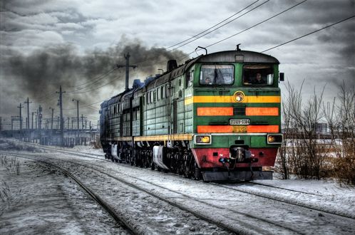 Обои на рабочий стол Локомотив темно-зеленого цвета едет по заснеженным рельсам в хмурый день
