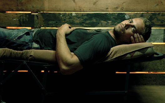 Обои на рабочий стол Актер Пол Уокер / Paul Walker лежит на раскладушке в сарае