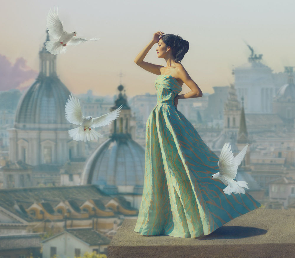 Обои для рабочего стола Девушка в длинном платье стоит в окружении голубей на фоне города, фотограф Svetlana Melik-Nubarova