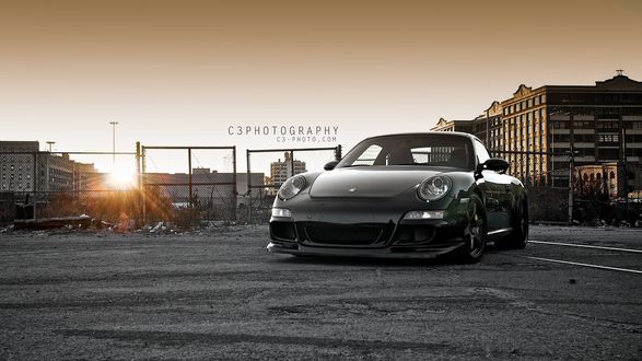 Обои на рабочий стол Черная Porshe 911 на фоне домов и неба