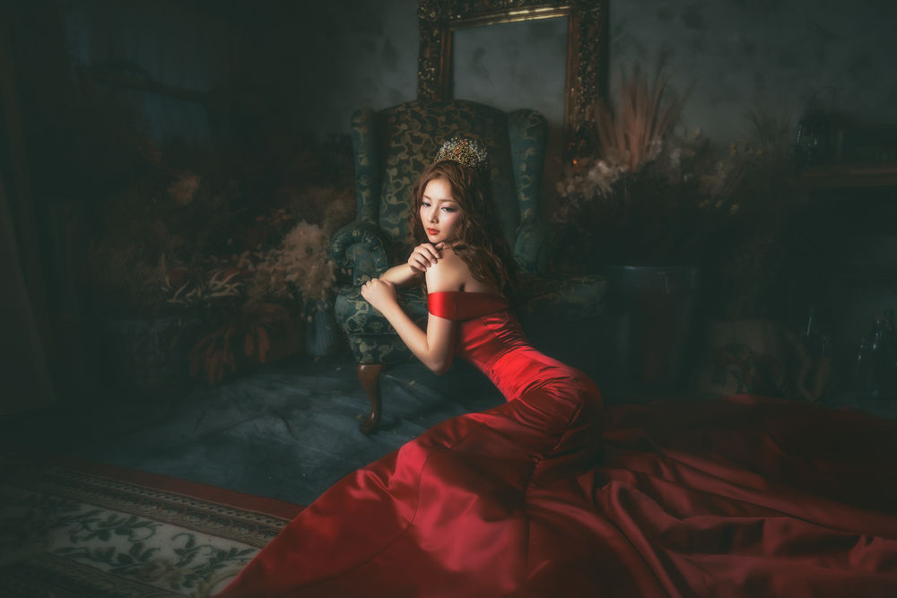Обои для рабочего стола Азиатка в красном платье и в короне сидит на ковре облокотившись на кресло
