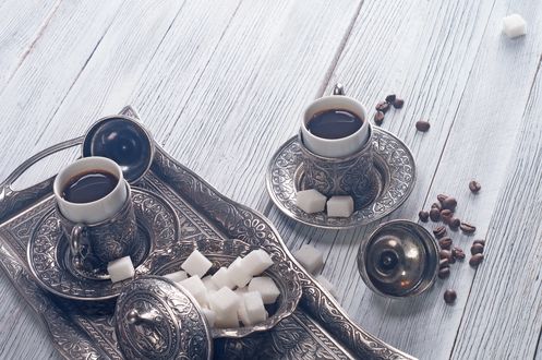 Обои на рабочий стол Чашка кофе и блюдце с сахаром на старинном подносе, рядом стоит еще одна чашка с кофе и лежат кофейные зерна