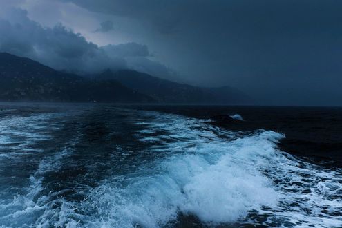 Обои на рабочий стол Темные волны моря, вдали виднеются горы