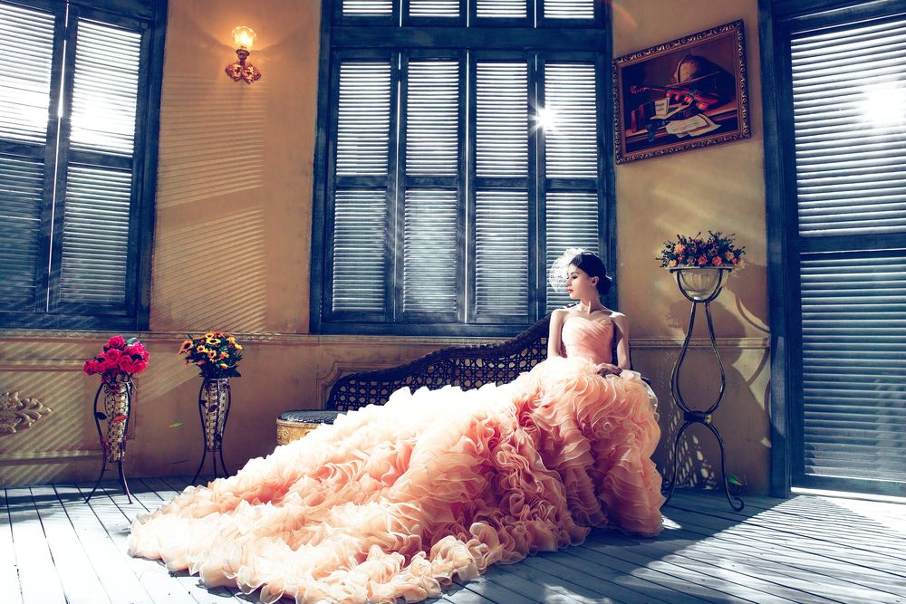 Обои для рабочего стола Азиатка в розовом бальном платье с пышной юбкой сидит на диване у окна, закрытого ставнями