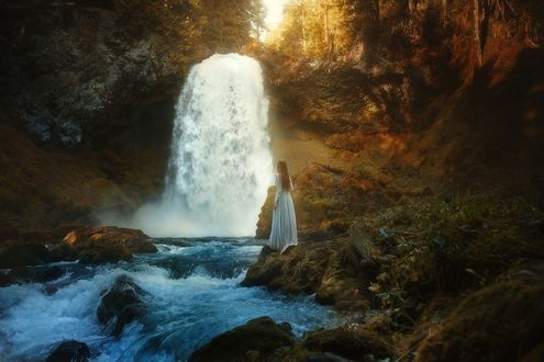 Обои на рабочий стол Девушка в длинном платье стоит у водопада, фотограф TJ Drysdale